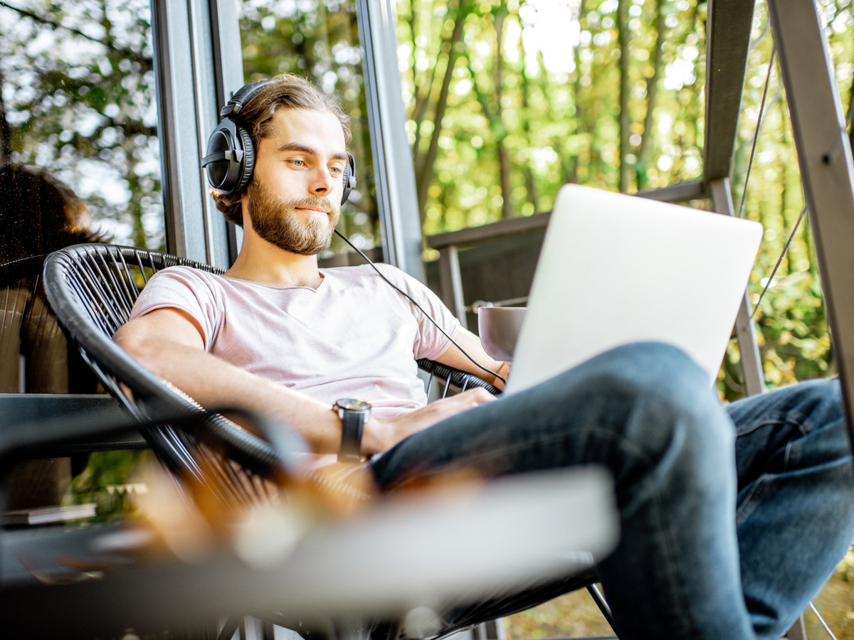 A digital nomad. A man wearing headphones with a laptop on his lap, sitting on a balcony