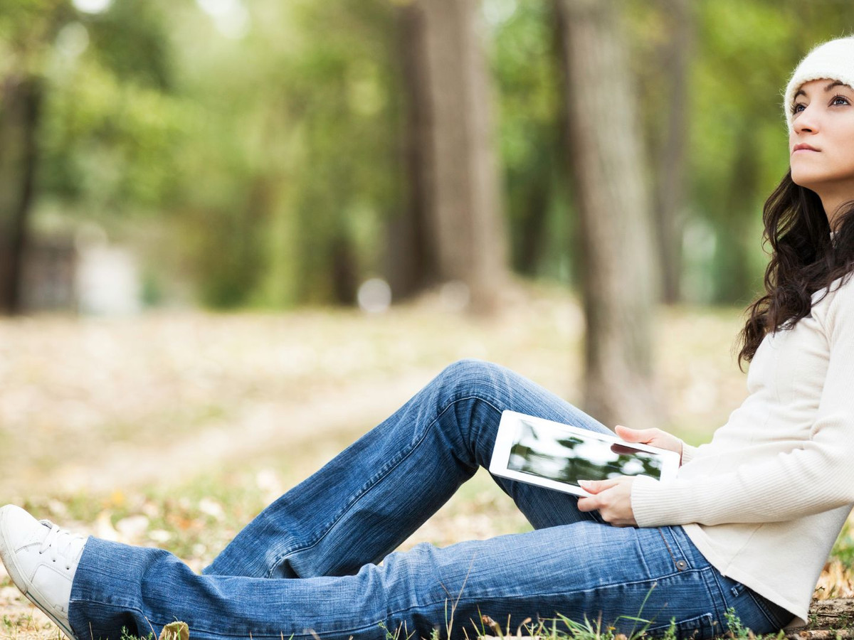 Woman sitting in the woods against a tree, daydreaming  with a magazine